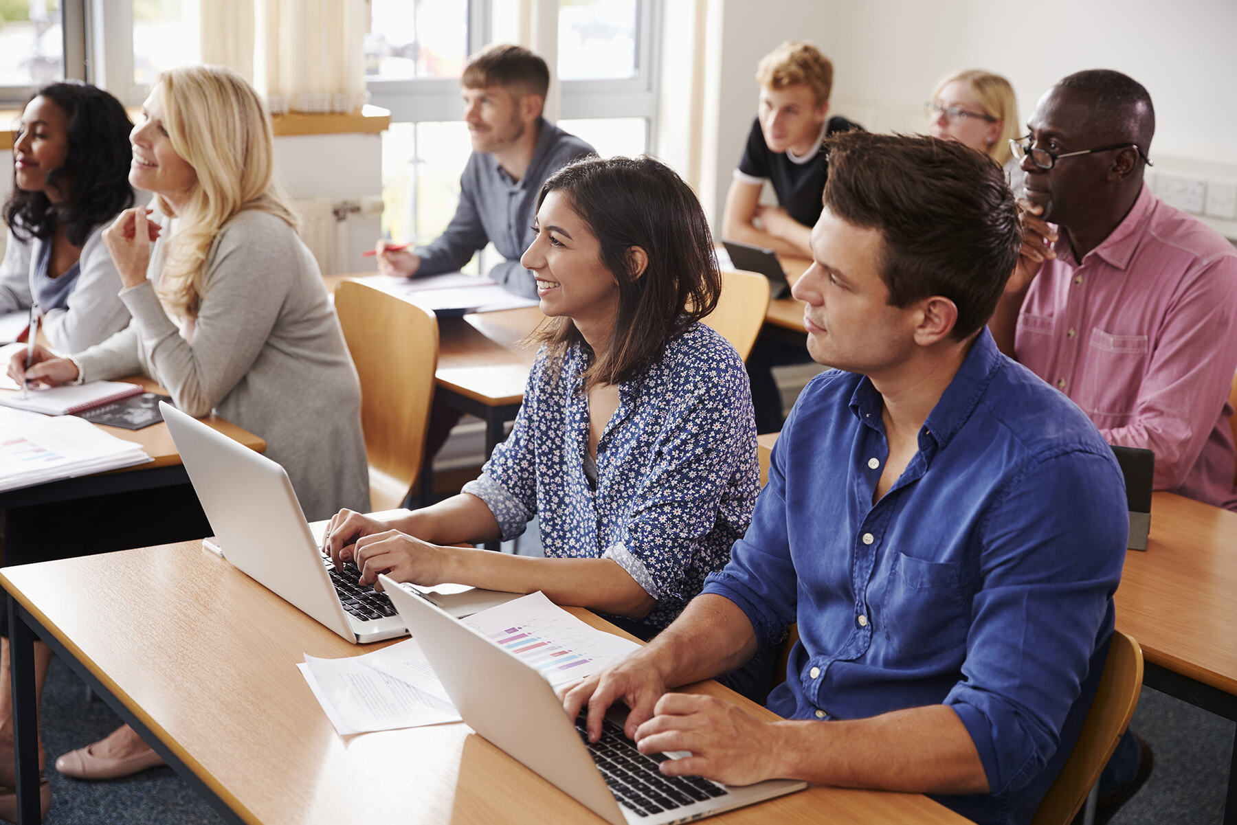 Adult learners working on laptops in a classroom
